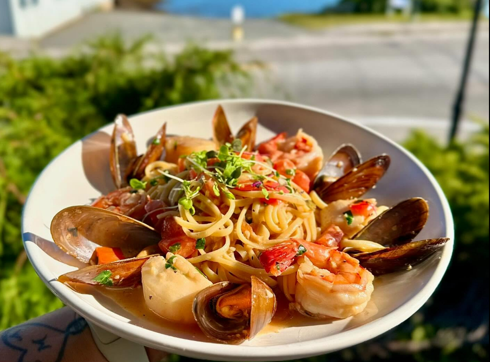 Seafood pasta with mussels and shrimp in a white bowl on a sunny outdoor table
