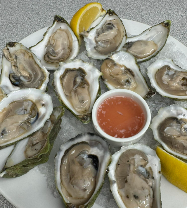Plate of raw oysters on ice with lemon wedges and a small cup of cocktail sauce