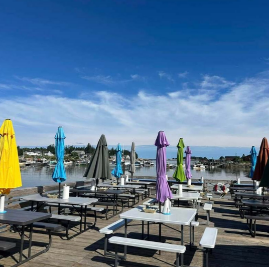 Colorful umbrellas and picnic tables on a seaside patio under a bright blue sky.