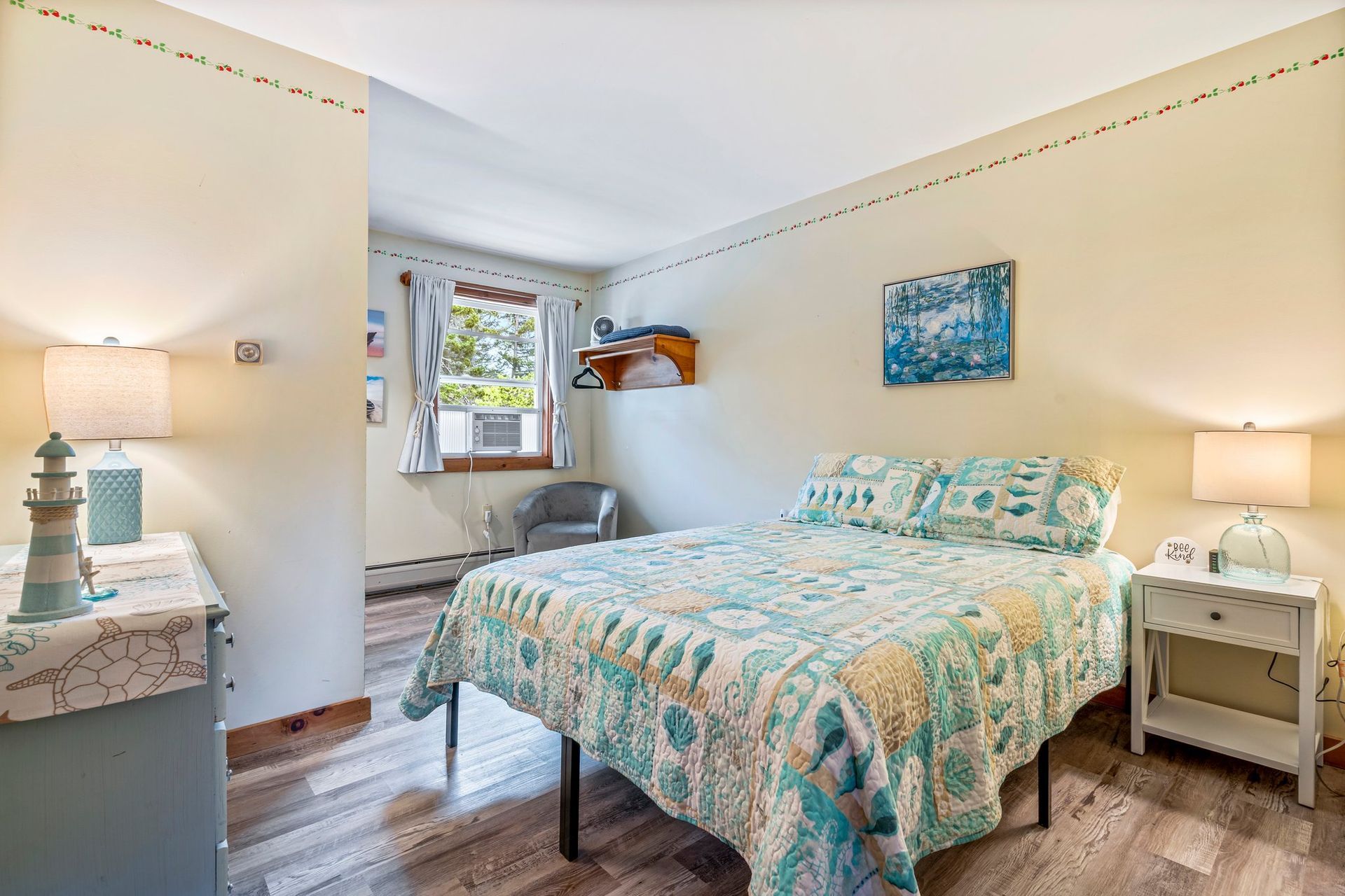 Bedroom with a light blue quilt, two bedside lamps, and a small window with a chair.
