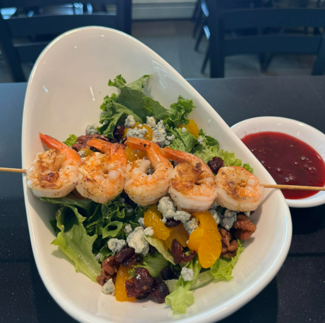 Grilled shrimp skewer over mixed greens with fruit and cheese, served with red dipping sauce.