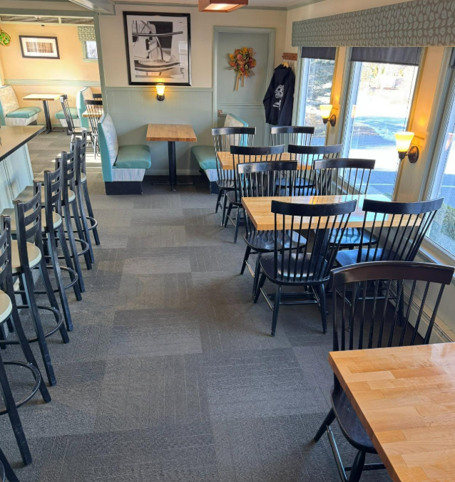 Empty café dining area with black chairs, wooden tables, and teal booths by bright windows
