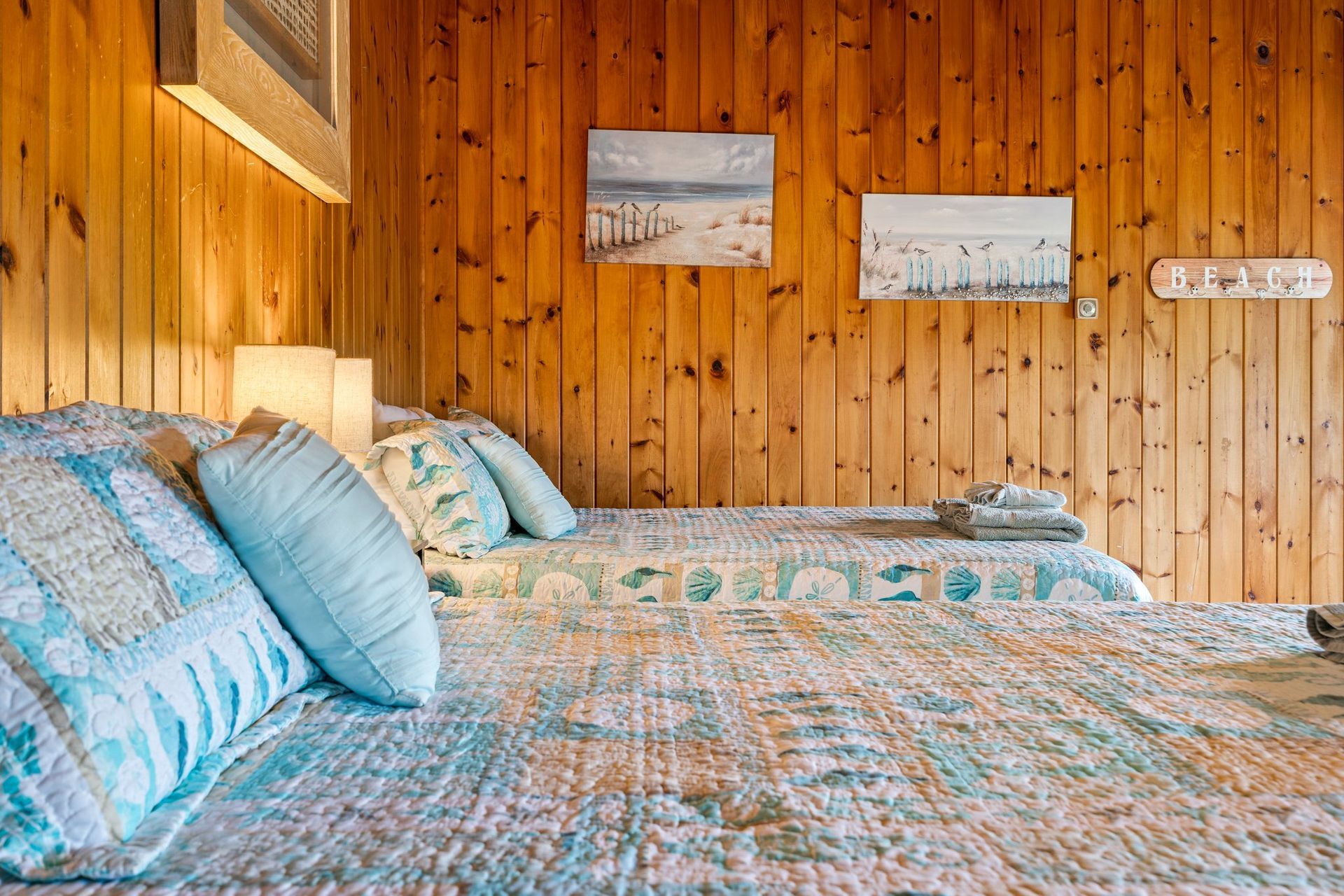 Cozy bedroom with twin beds, blue patterned bedding, and wood-paneled walls.