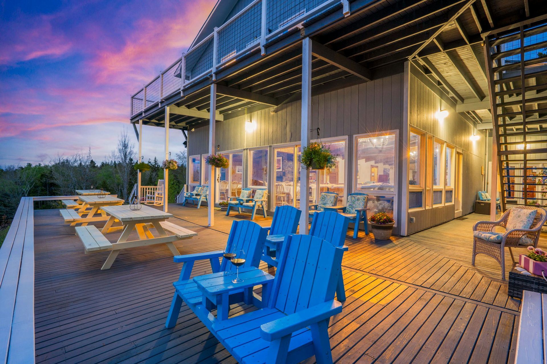 Patio deck with blue chairs and tables outside a modern house at sunset, lit warmly inside