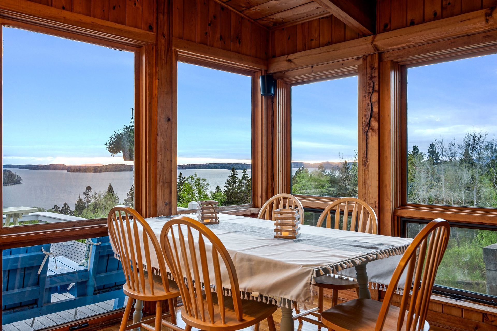 Wooden porch dining area overlooking a lake, with chairs and a table by large open windows.