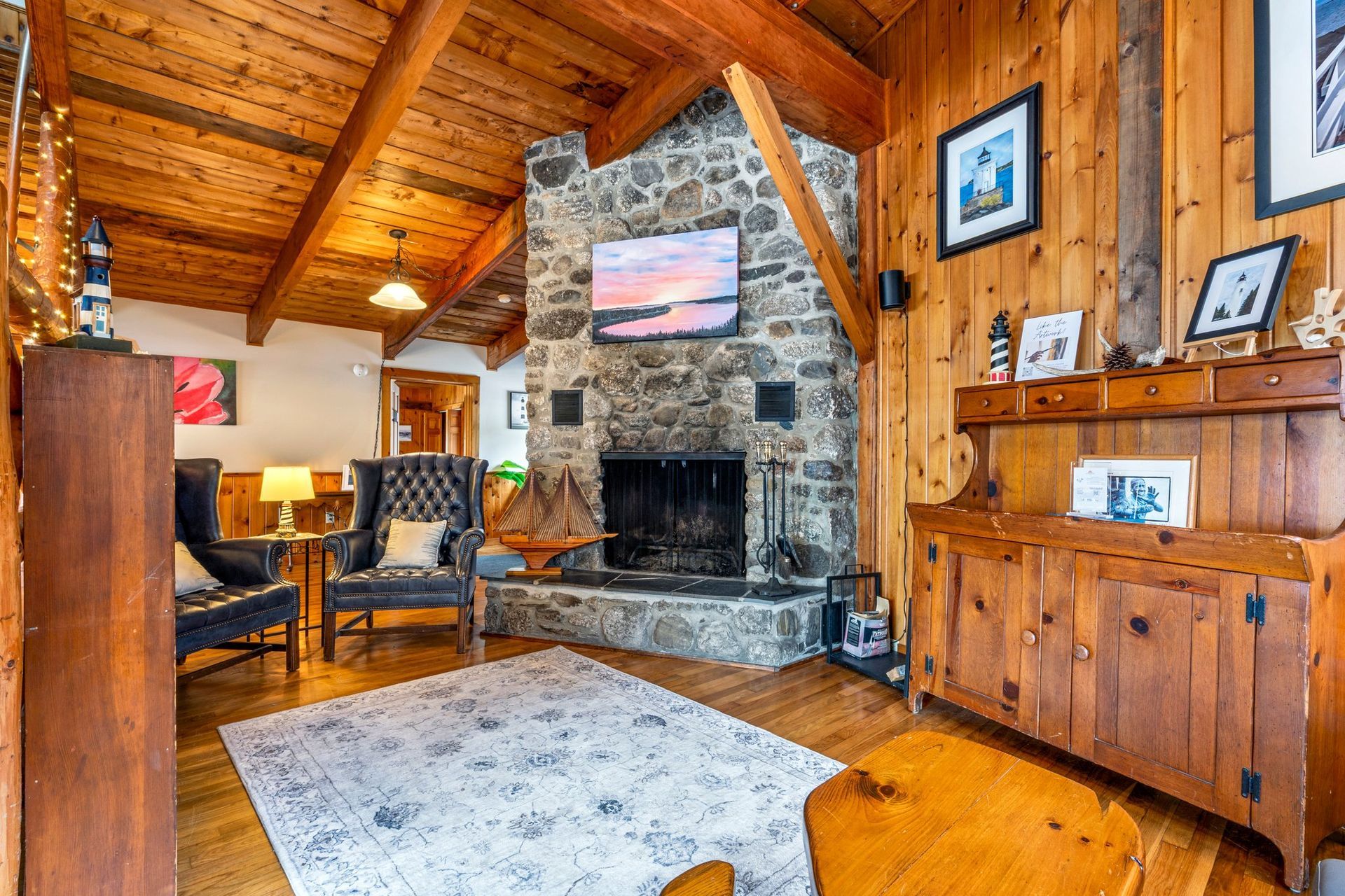 Cozy log cabin living room with stone fireplace, wood-paneled walls, and vaulted ceiling