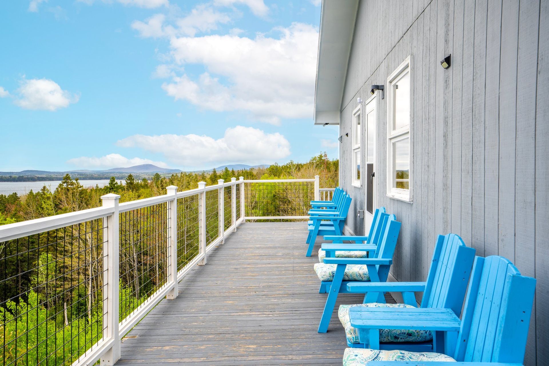Blue chairs on a white porch overlooking water and trees