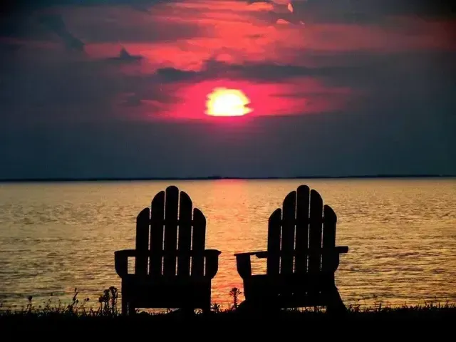 Two adirondack chairs are silhouetted against a sunset over the Lake Erie Sunset at Scenic Rock Ledge Inn