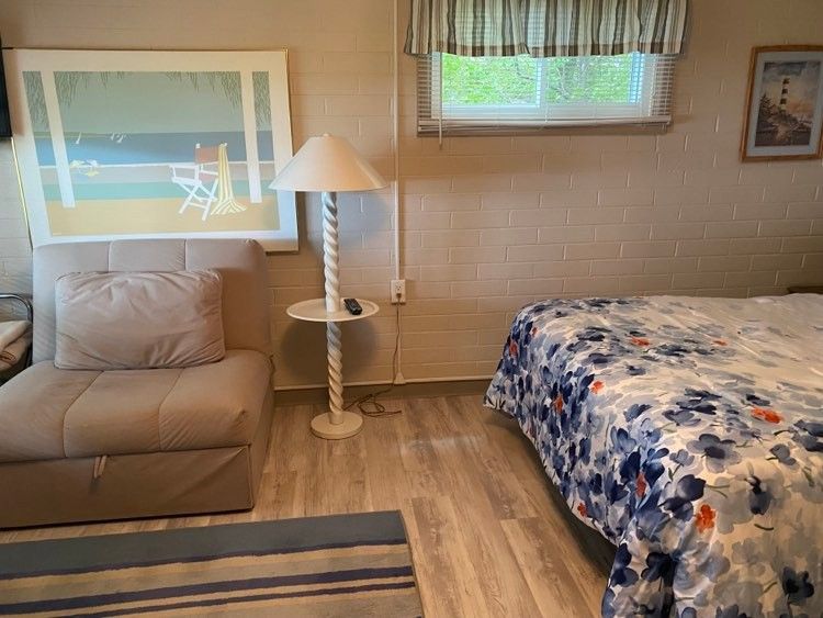 A bedroom with a bed , chair , lamp and picture on the wall.