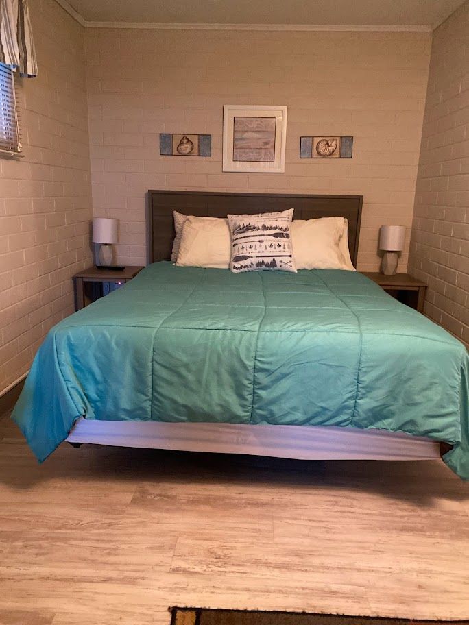 A bed with a blue comforter and pillows in a small bedroom.