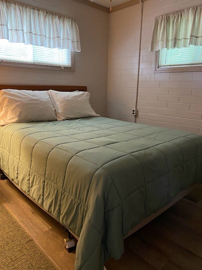 A bed with a green comforter and white pillows in a bedroom.