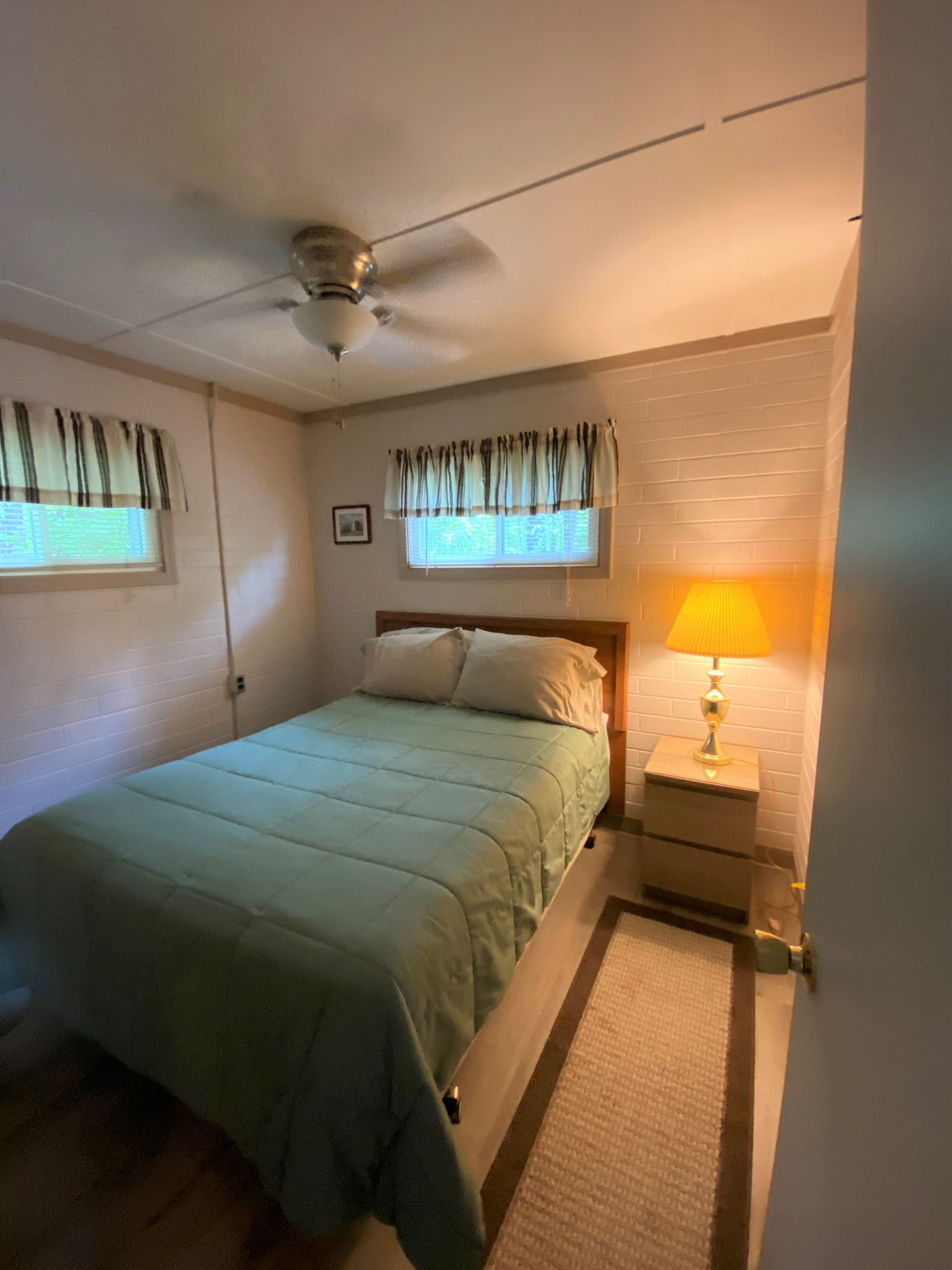 A bedroom with a bed , nightstand , lamp and ceiling fan.
