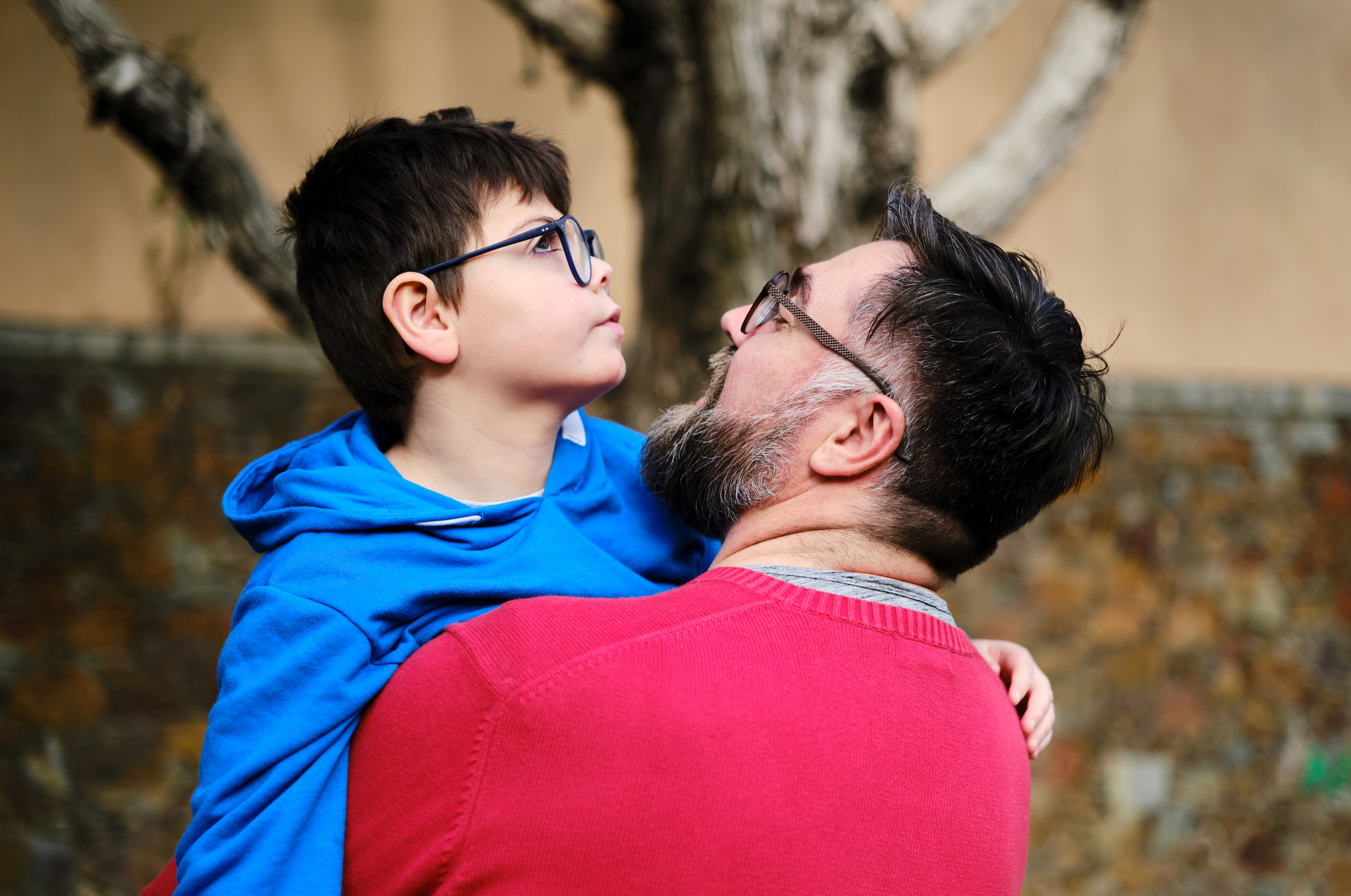 A man in a red sweater is holding a young boy in his arms.