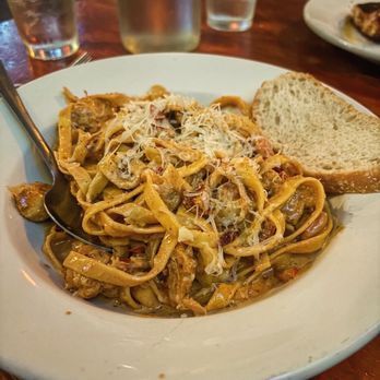 Plate of tagliatelle pasta with meat sauce and grated cheese, served with a slice of bread.