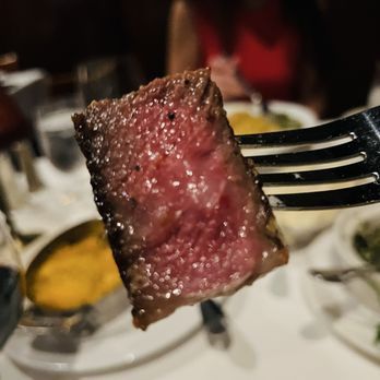 Medium-rare seared steak cube on a fork above a restaurant table setting