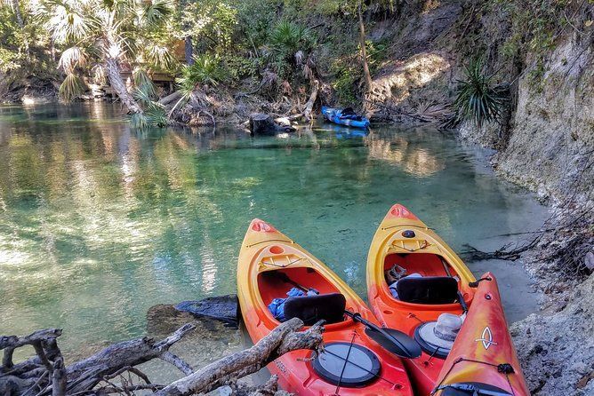Two orange kayaks on a clear river beside a rocky, wooded bank