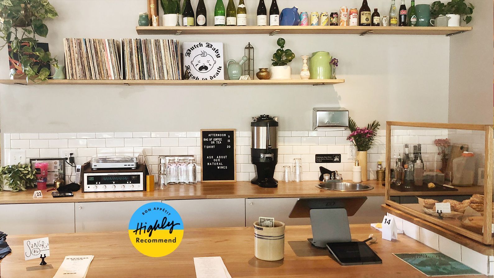 Bright café counter with coffee machine, pastries, shelves, and a small display case in a cozy interior.