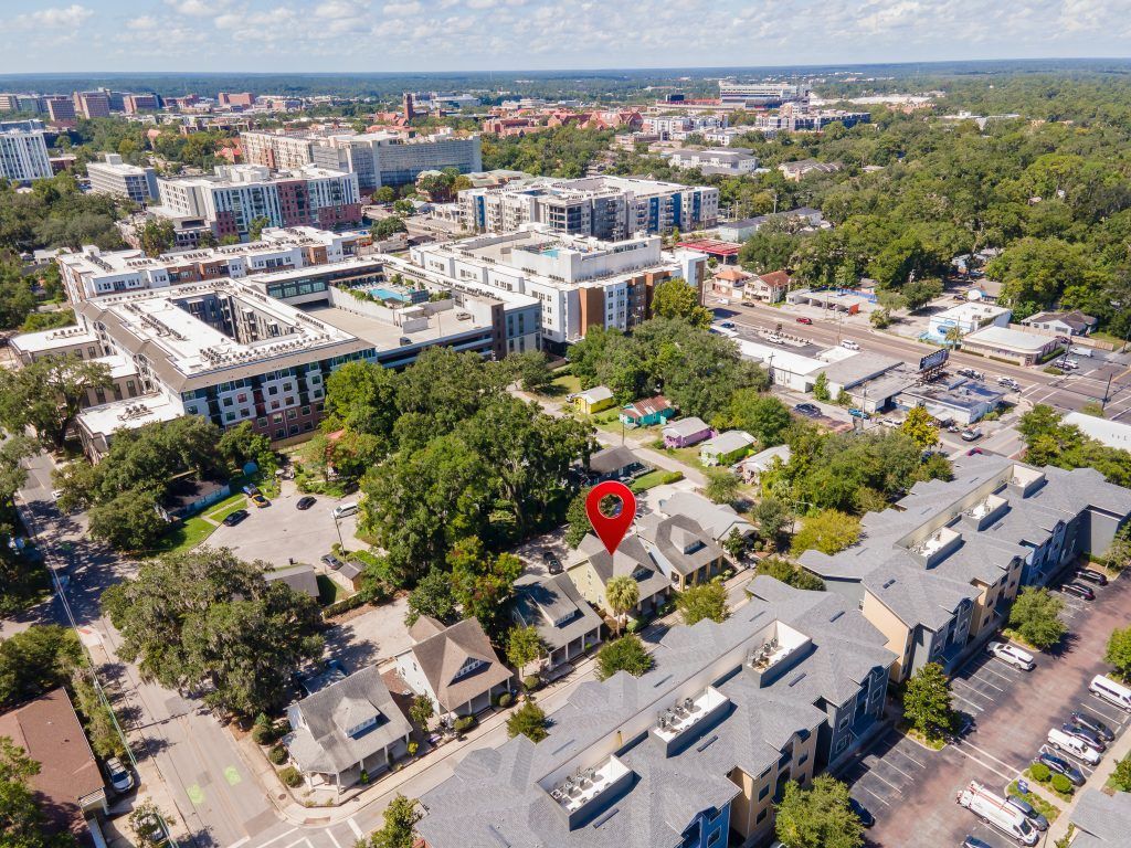 Aerial view of a suburban neighborhood with houses, trees, streets, and a red location pin over one home
