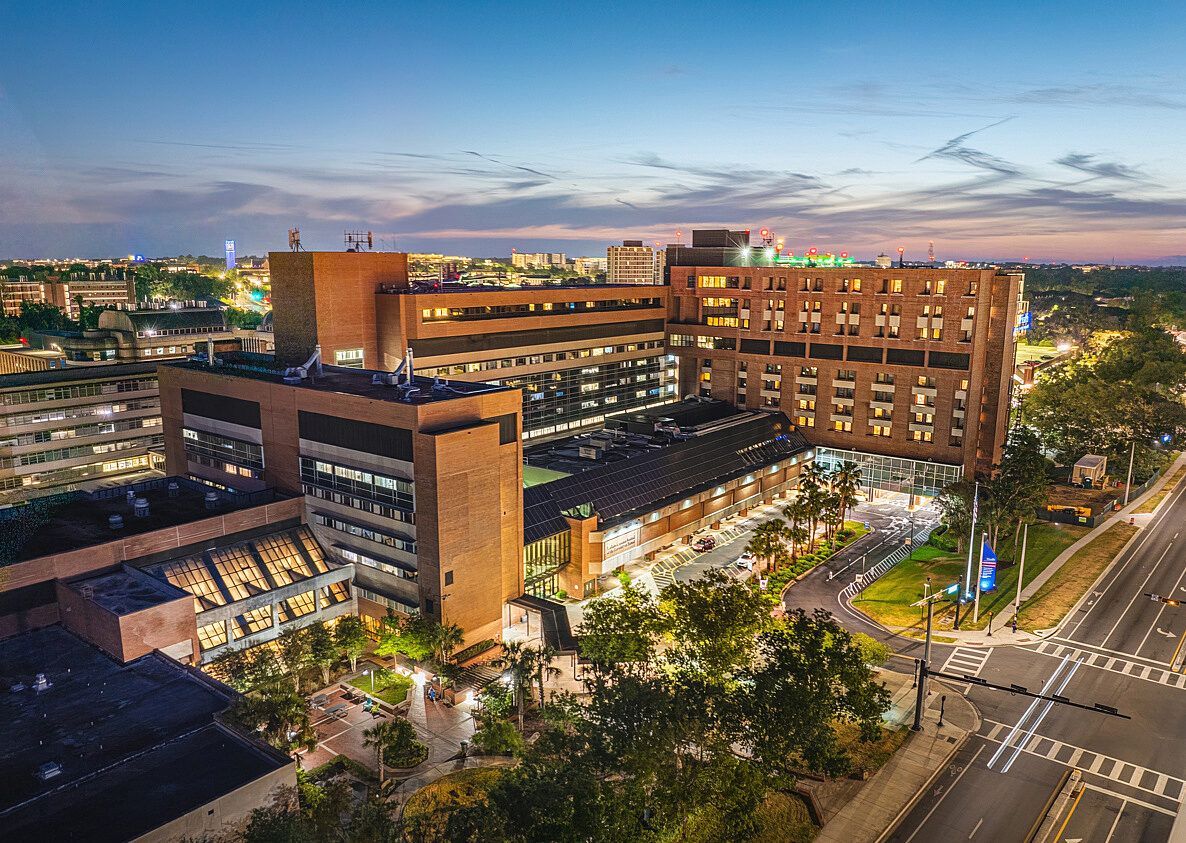 Aerial view of a lit brick building at dusk beside a city street and trees