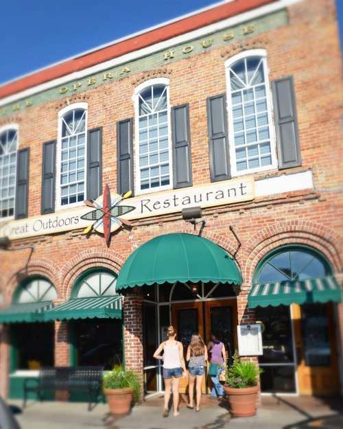 Brick restaurant storefront with green awnings and two people standing outside