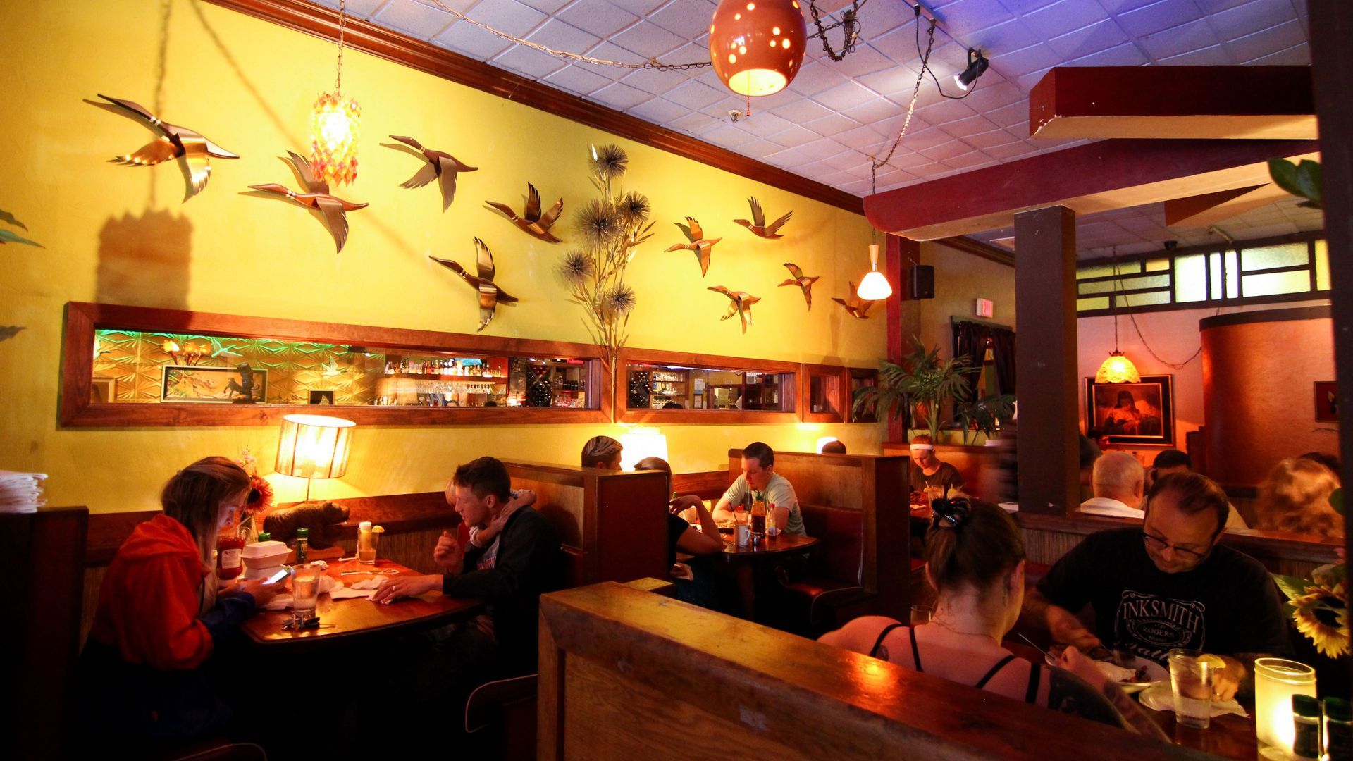 Warm, dimly lit restaurant with diners seated at tables and decorative bird wall art