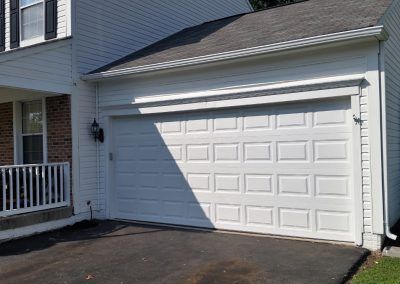 A white garage door is sitting in front of a white house.