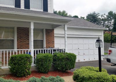 A white truck is parked in front of a brick house with a porch.