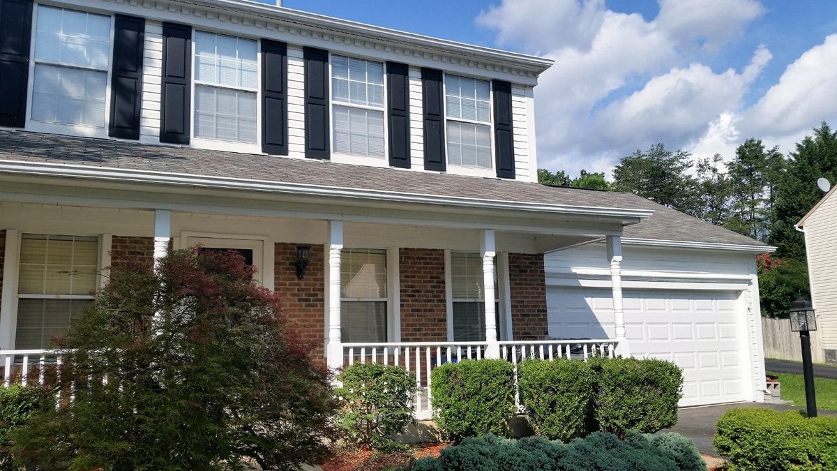 A white house with black shutters and a porch on a sunny day.