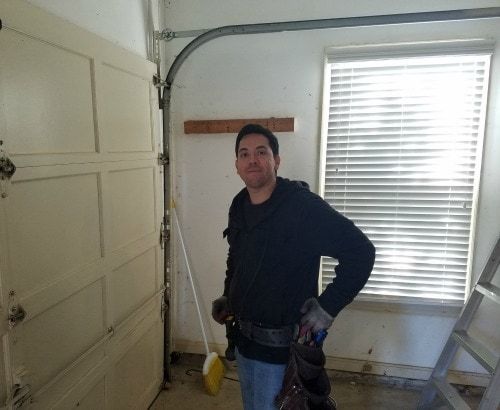 A man is standing in front of a garage door holding a broom.