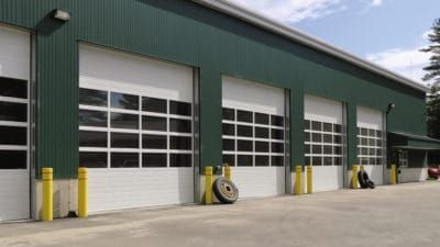 a row of white garage doors on a green building .