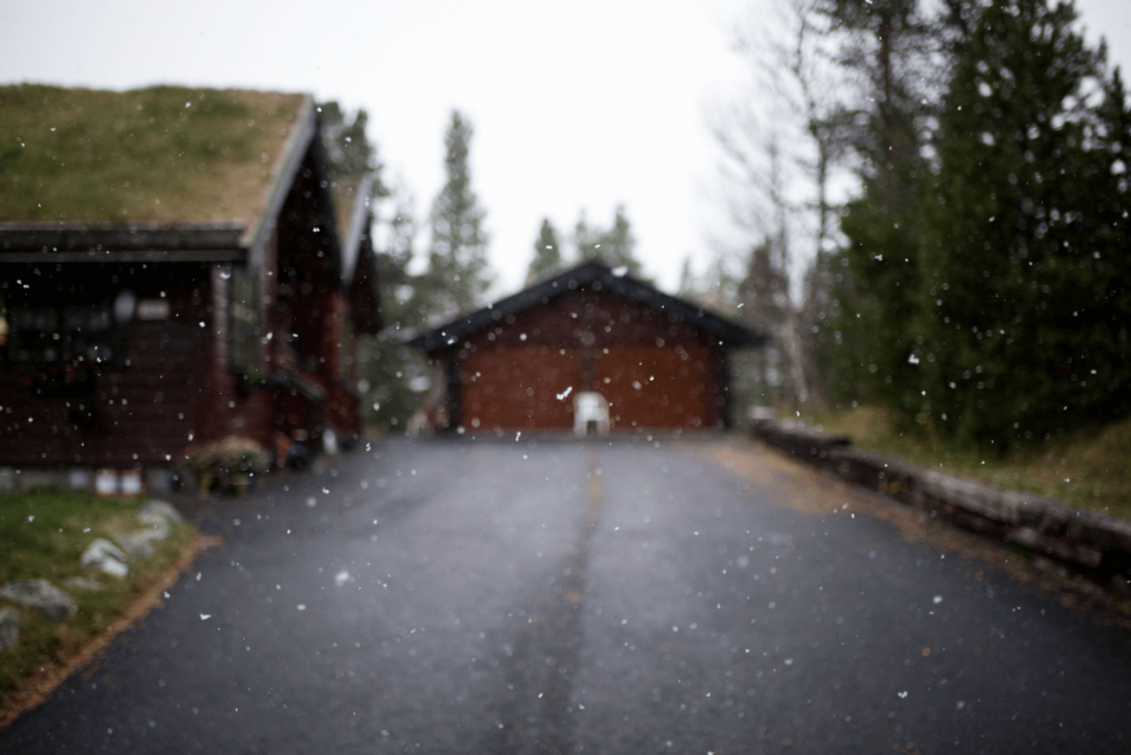 A snowy road leading to a house with a green roof.