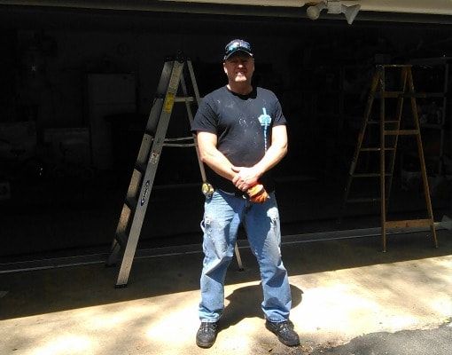a man is standing in front of a garage door with a ladder in the background .