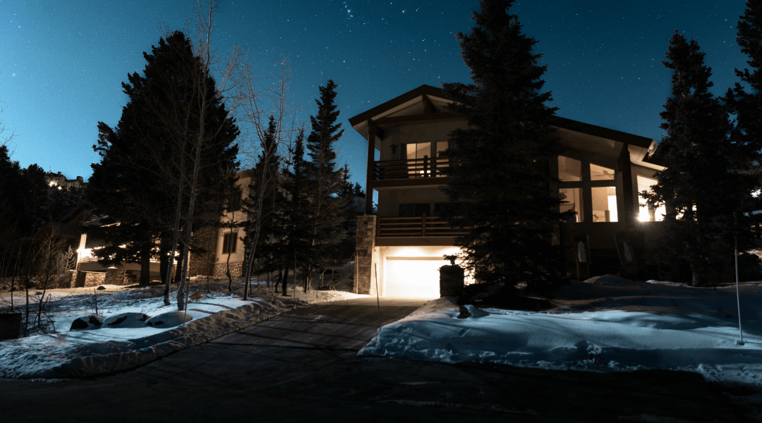 A large house is lit up at night in the middle of a snowy forest.