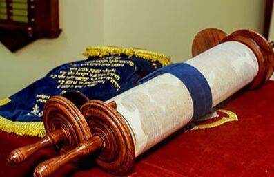 Torah scroll on a red cloth beside a blue velvet cover with gold embroidery