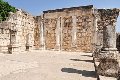 Ancient stone ruins with a carved wall, columns, and an open courtyard in sunlight