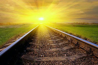 Sunlit railroad tracks stretching toward the horizon under a bright yellow sunset sky