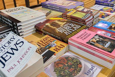 Stacked books and magazines on a table, including travel, religion, and history titles.