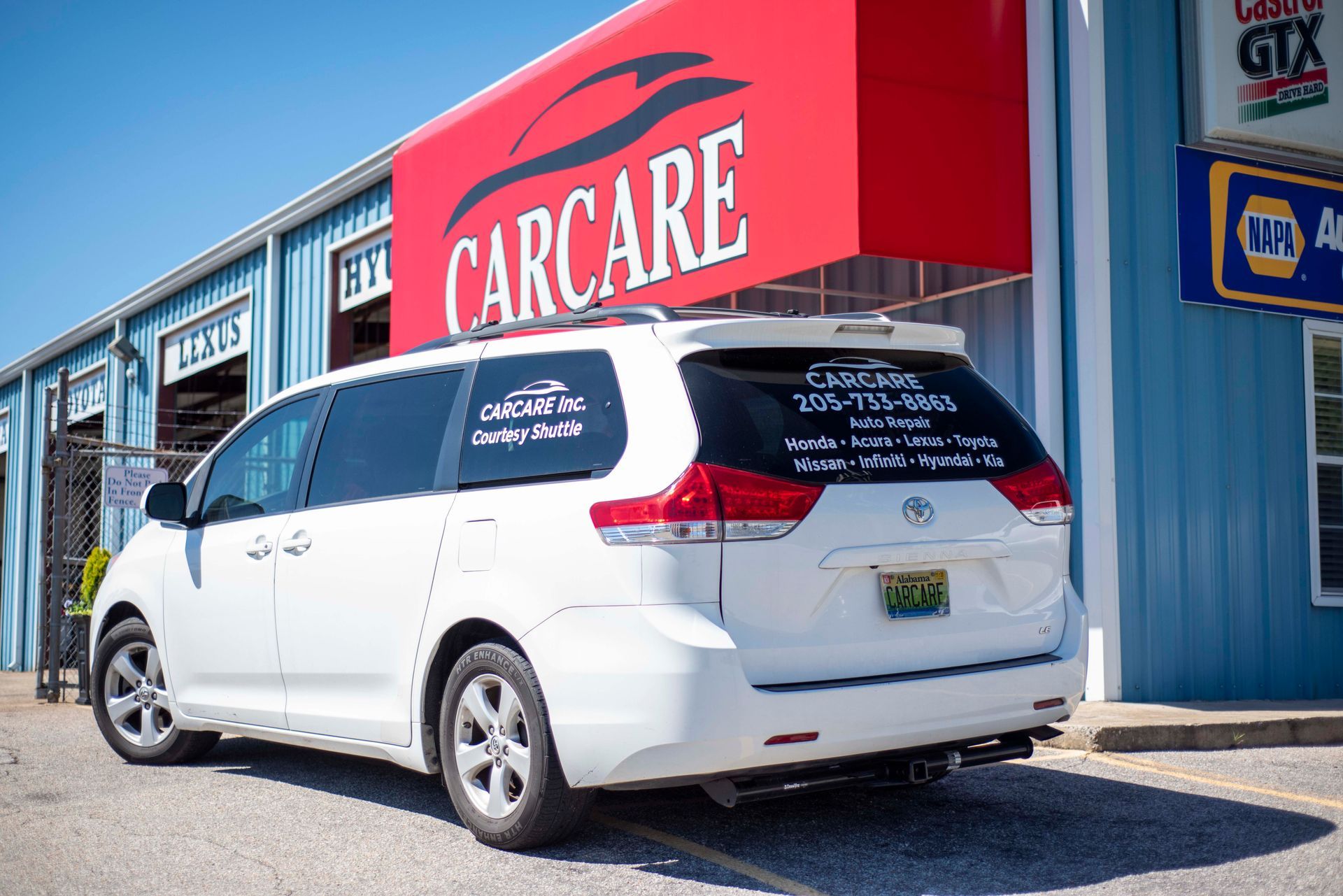 White minivan parked outside a CARCARE auto shop with a red sign and blue building exterior