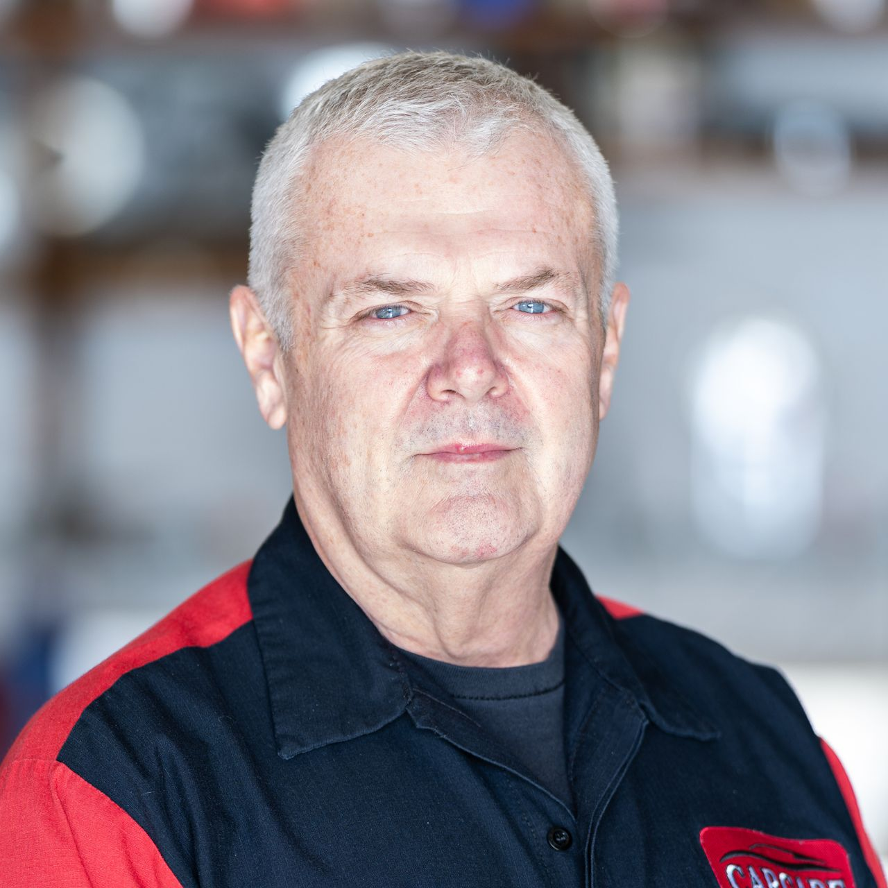 Portrait of a man in a black and red collared shirt against a blurred indoor background