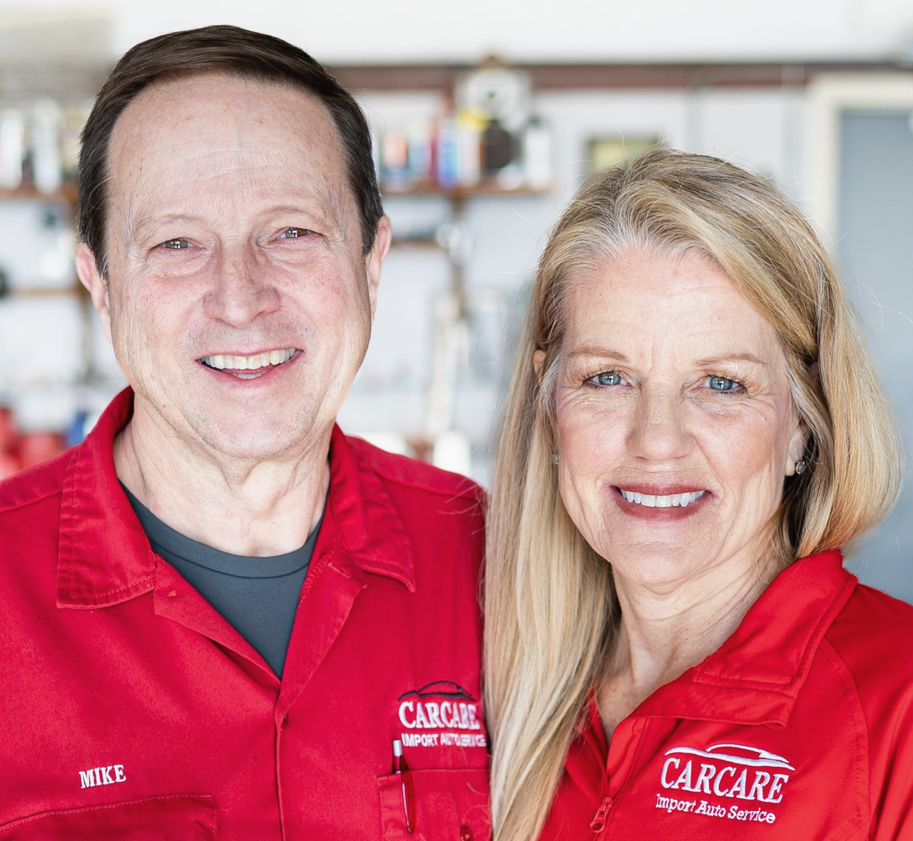 Two smiling CarCare employees in red shirts standing indoors