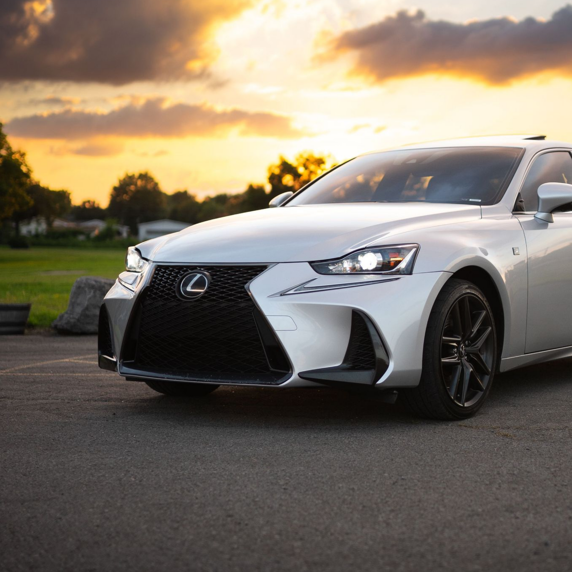 White Lexus sedan parked on a road at sunset, with trees and a glowing sky in the background
