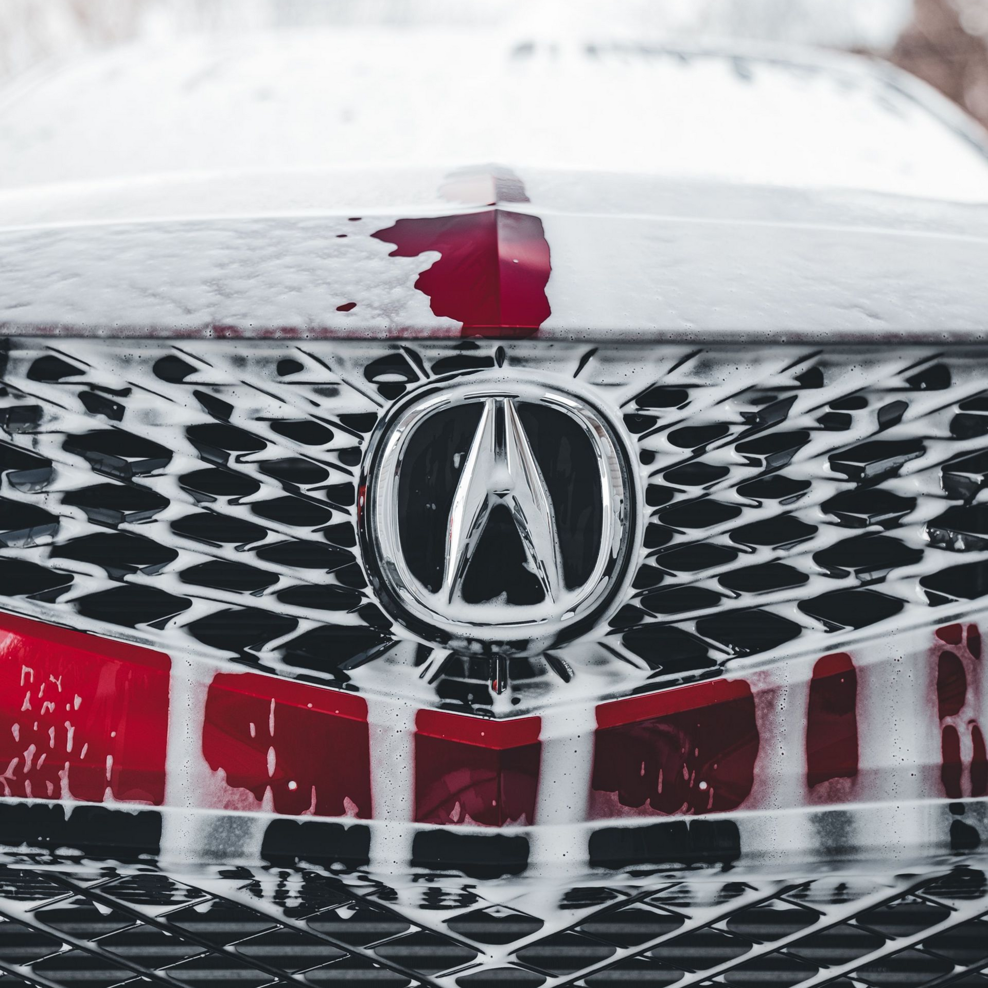 Close-up of an Acura grille and emblem covered in snow, with red accents visible underneath.