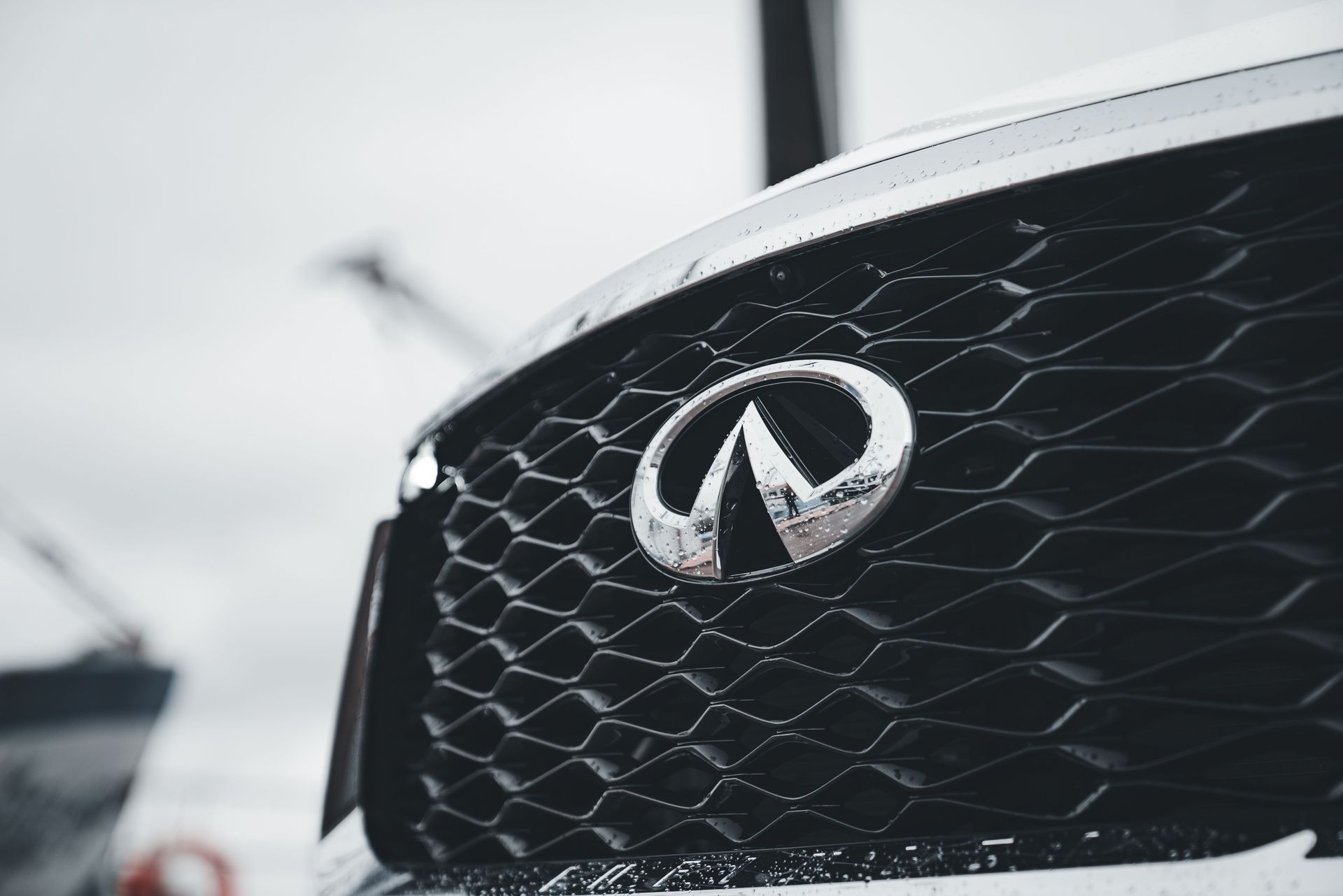 Close-up of an Infiniti car grille with chrome emblem against a blurred outdoor background