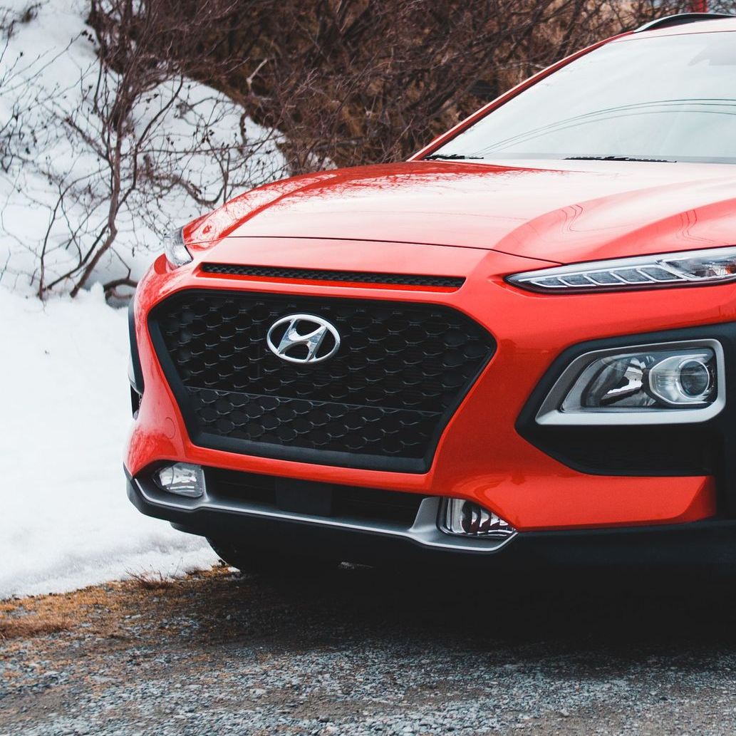 Red Hyundai car front parked by snow on a wet road