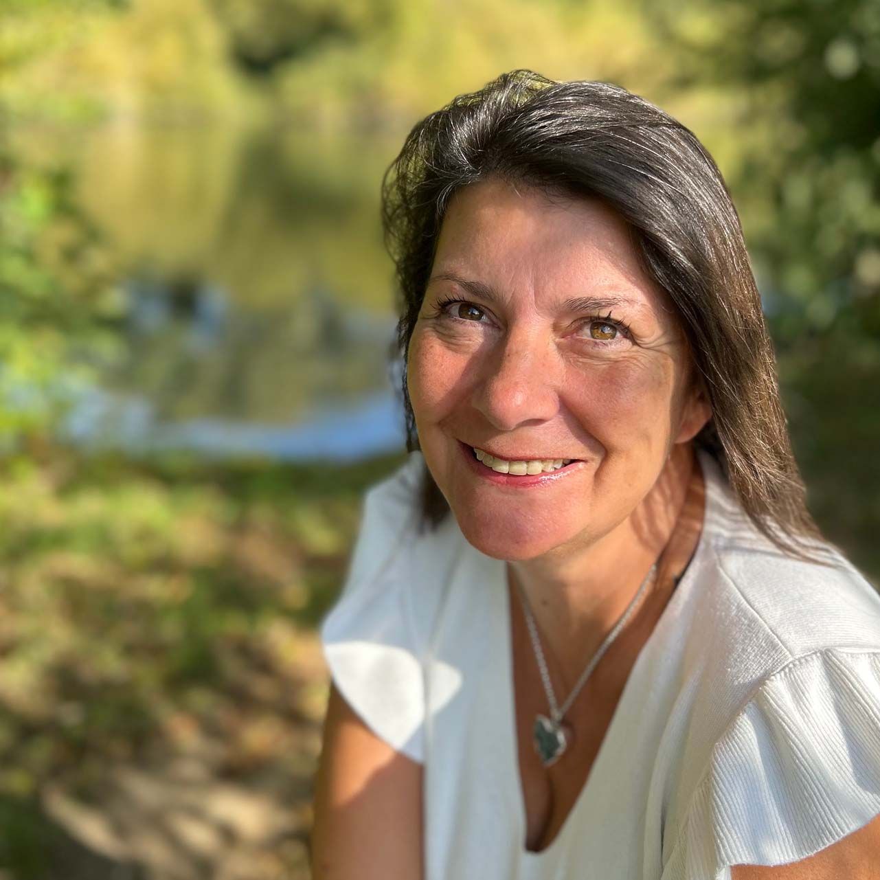 a woman wearing a white shirt and a necklace is smiling for the camera .