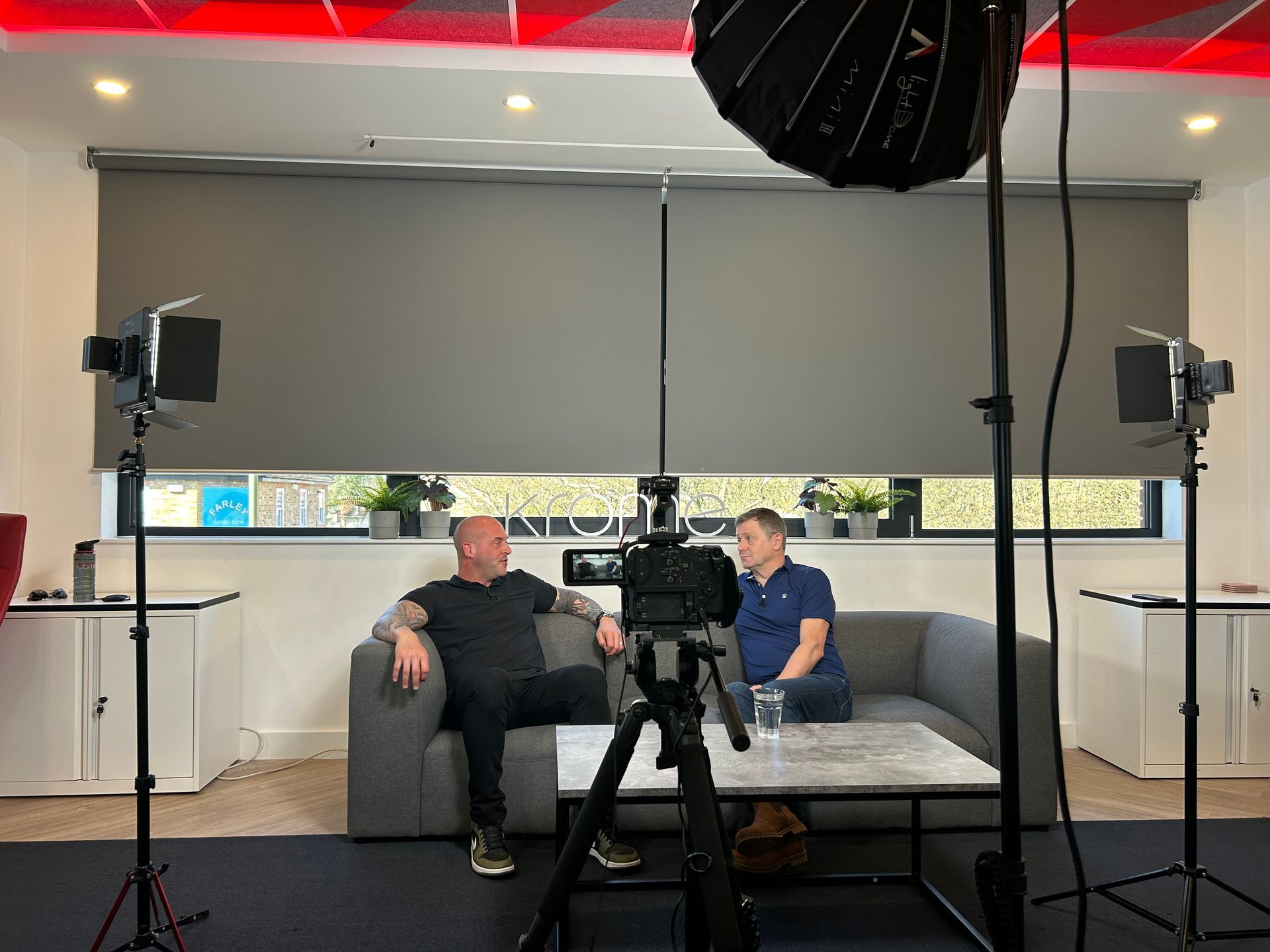 Two men are sitting on a couch in front of a camera.