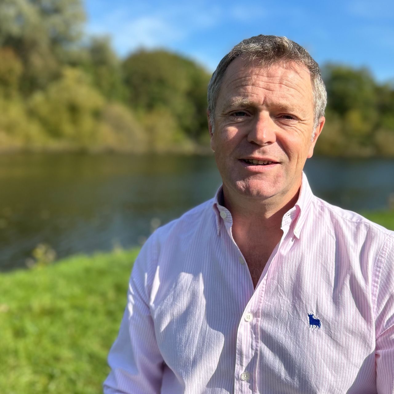 a man wearing a pink shirt with a blue horse on the sleeve is standing in front of a body of water .