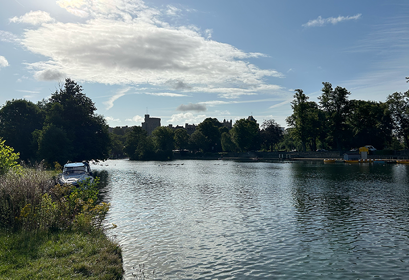 A large body of water surrounded by trees on a sunny day with Windsor Castle in the background