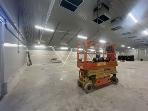 Interior of a large warehouse; orange scissor lift in the foreground, white walls, and a concrete floor.