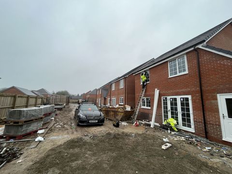 Construction workers on a brick house under overcast skies, mud, vehicle, and debris present.